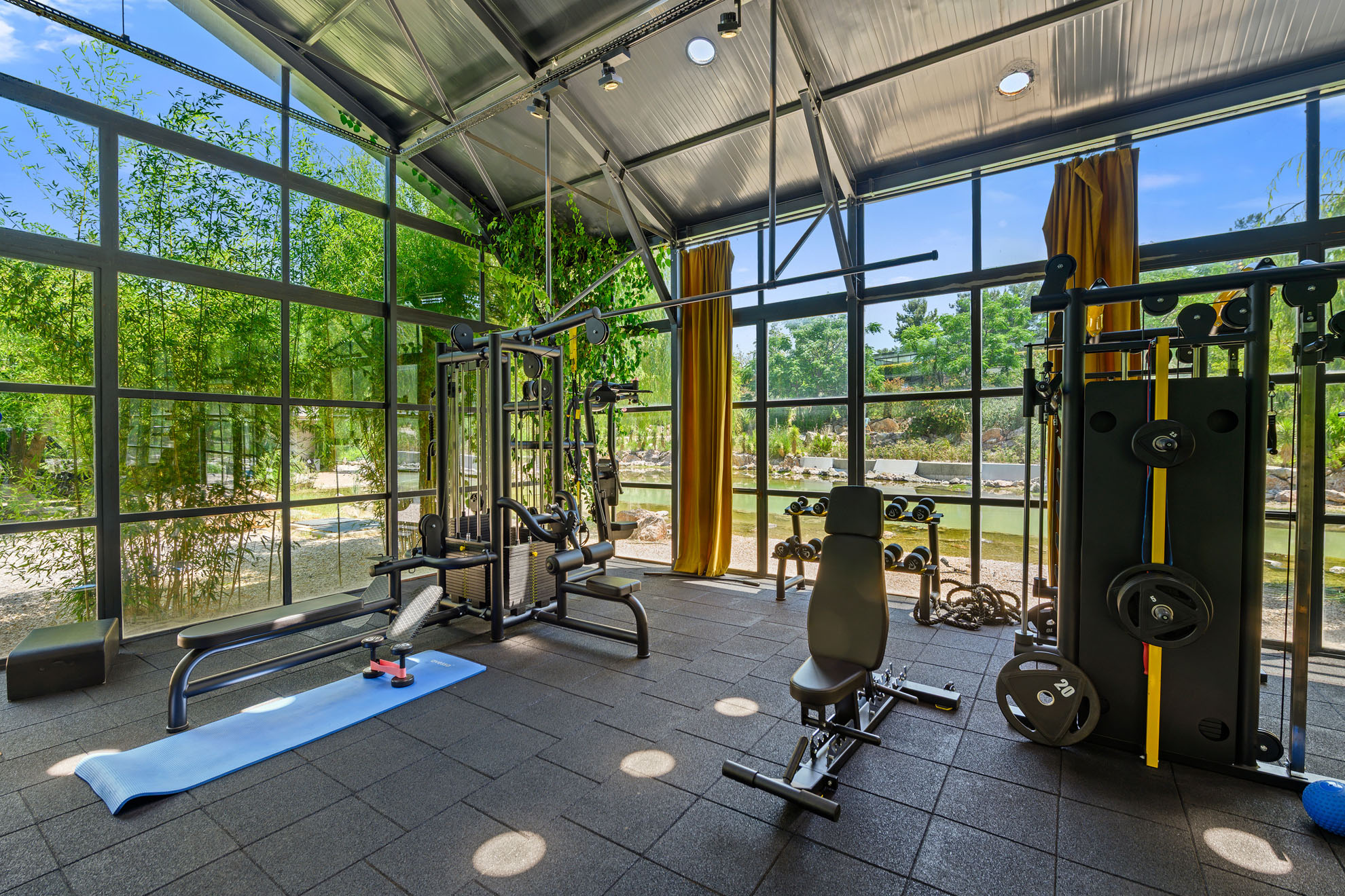 İzmir Urla'daki villanın geniş cam cepheli, gölet manzaralı ve yüksek tavanlı modern spor salonunda profesyonel fitness aletleri bulunuyor.