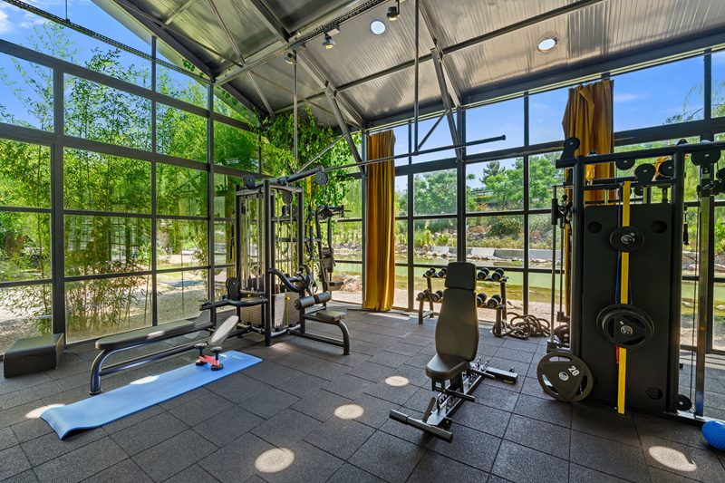 İzmir Urla'daki villanın geniş cam cepheli, gölet manzaralı ve yüksek tavanlı modern spor salonunda profesyonel fitness aletleri bulunuyor.
