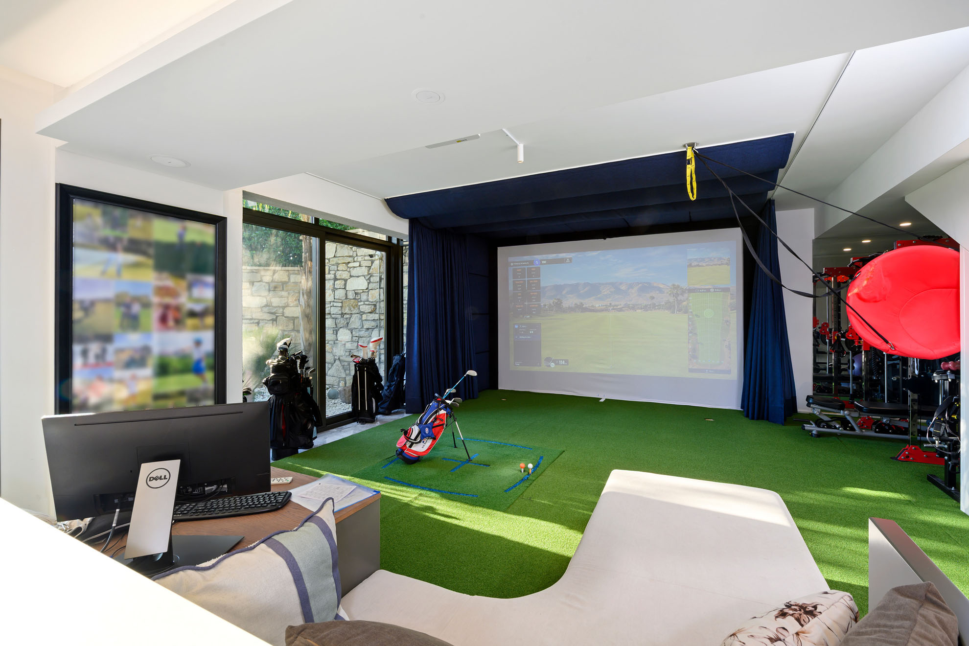 Urla'daki lüks bir villanın yeşil suni çimli ve büyük projeksiyon ekranlı, aydınlık kapalı golf simülatörü odasının mimari fotoğrafı.