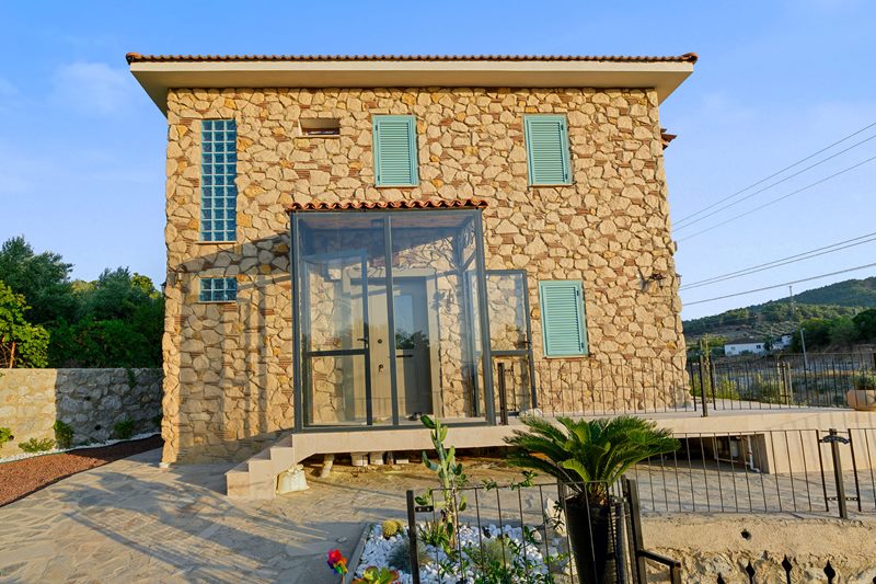 İzmir Torbalı'daki doğal taş ev, altın saatte turkuaz panjurları ve modern cam girişiyle huzurlu bir emeklilik yaşamını yansıtıyor.