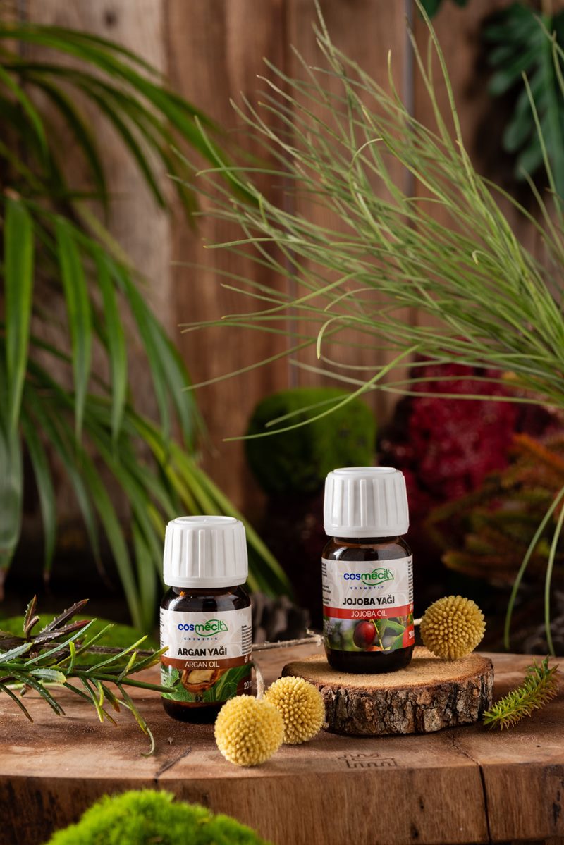 Mecitefendi stüdyo çekiminde ahşap kütük üzerinde doğal Cosmecit argan yağı ve jojoba yağı şişeleri.