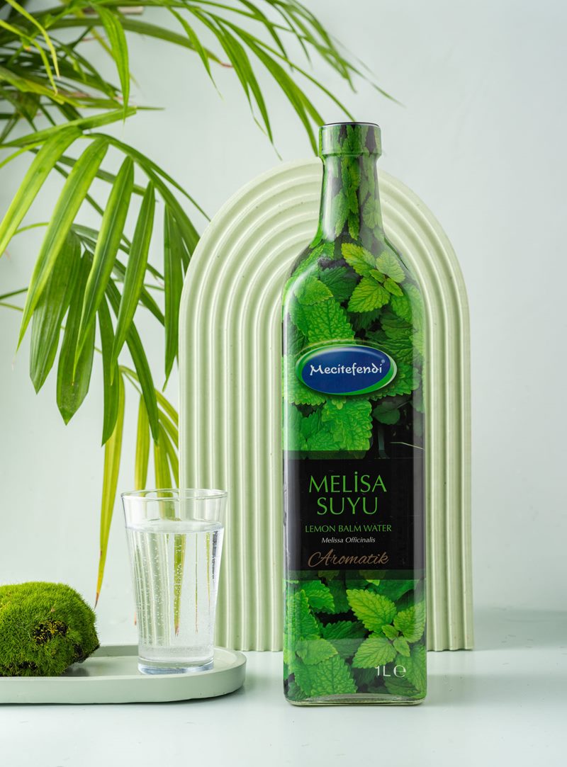 Mecitefendi konsept stüdyo çekiminde yeşil kemer önünde doğal aromatik melisa suyu ve su bardağı.
