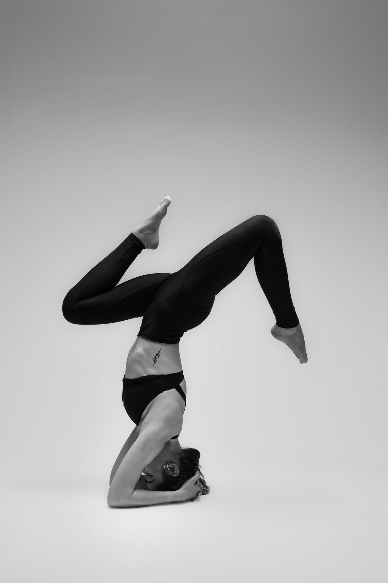 İzmir stüdyosunda yoga eğitmeni Melis'in (@yogawithmelis) gri fon önünde siyah beyaz asana pozuyla sergilediği estetik ve güçlü yoga duruşu.