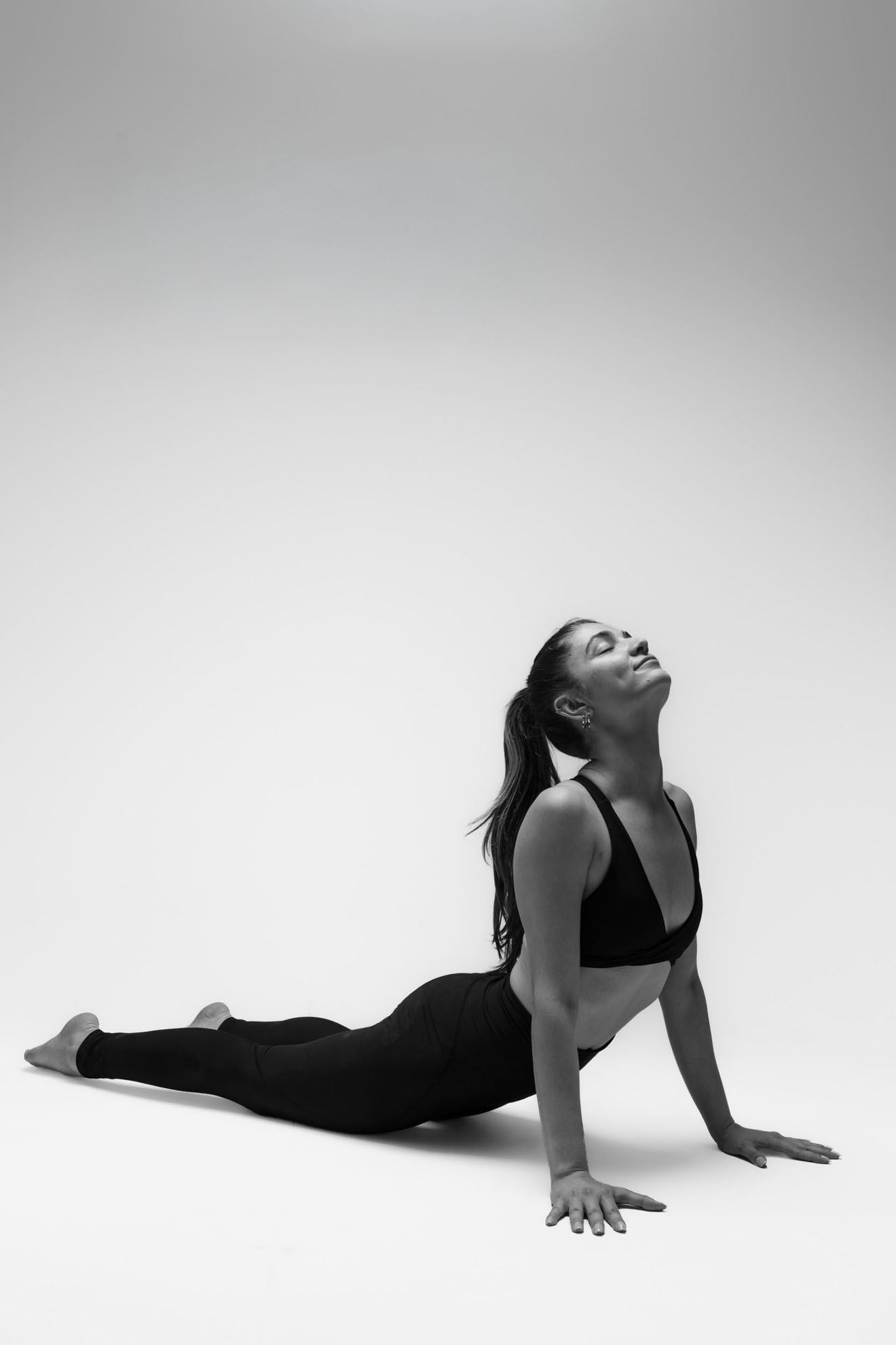 İzmir'deki stüdyoda gri fon önünde siyah kıyafetiyle asana duruşu yapan yoga eğitmeni yogawithmelis esnekliğini sergiliyor.