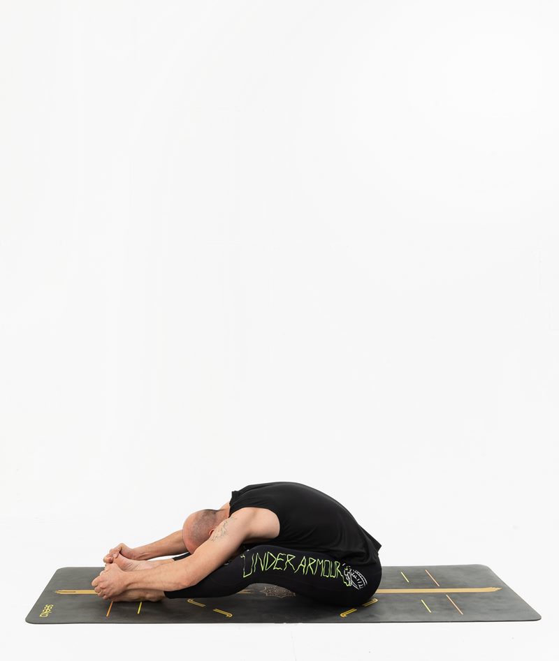 İzmir stüdyo matında erkek eğitmenin oturarak öne katlanma duruşunu uyguladığı Kentli Gurular yoga fotoğraf çekimi.
