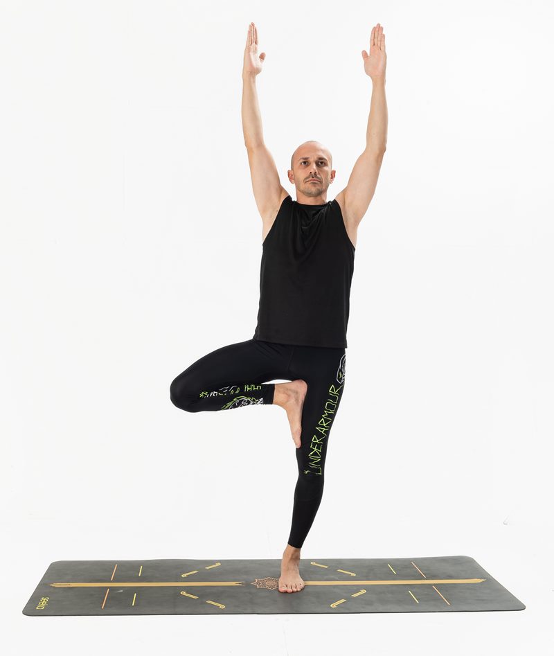 İzmir stüdyo zemininde erkek eğitmenin kollarını yukarı açarak ağaç duruşu yaptığı Kentli Gurular yoga fotoğraf çekimi.