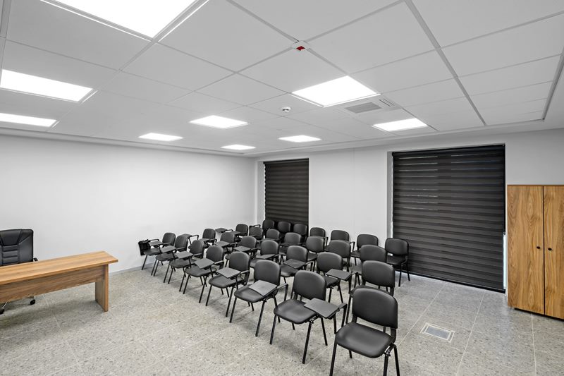 Geniş açıyla itfaiye eğitim salonu: 60x60 asma tavan, LED panel dizisi, eğitmen masası ve ahşap dolap.