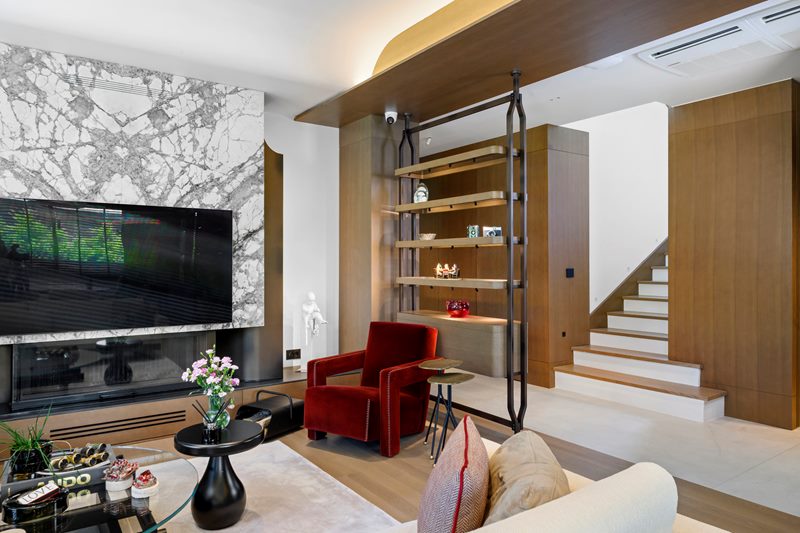 Özel villa salonunda mermer kaplı TV ünitesi, metal çerçeveli ahşap raflar ve kırmızı berjerler, geniş açı.