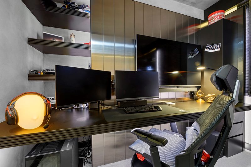 Villanın oyun ofisinde çift monitörlü masa, oyuncu koltuğu, koyu ahşap raflar ve duvar TV'si, HDR tekniğiyle.