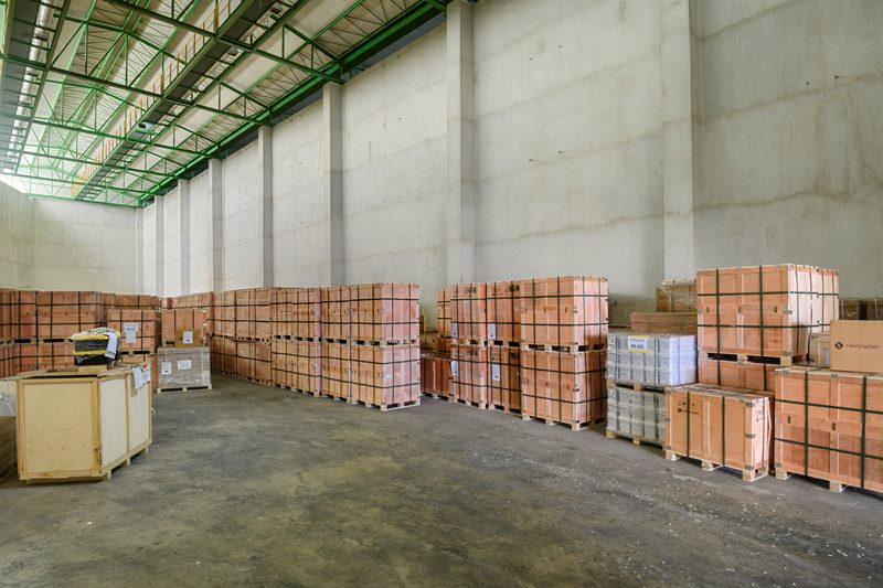 Ahşap sandıkların duvar boyunca sıralandığı antrepo deposu, yüksek beton duvarlar ve çelik çatı konstrüksiyonu.