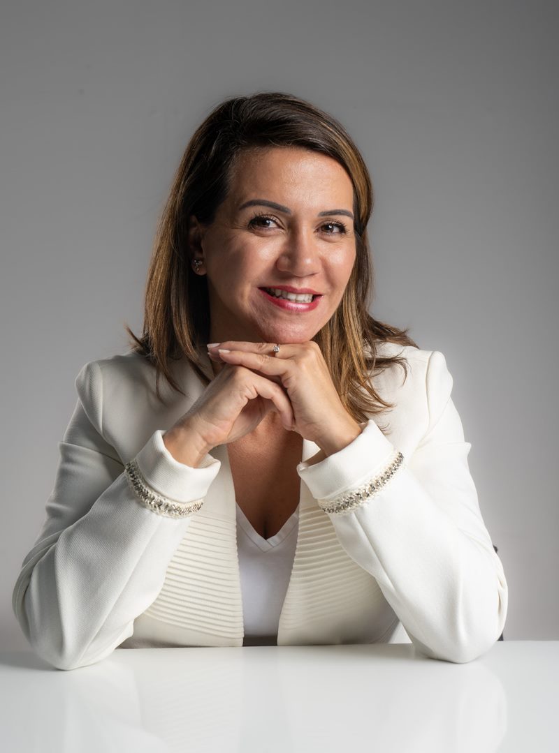Dilara Karaçoban için kişisel marka fotoğraf çekimi kapsamında beyaz masada elleri kenetli aydınlık tebessümlü renkli portre.