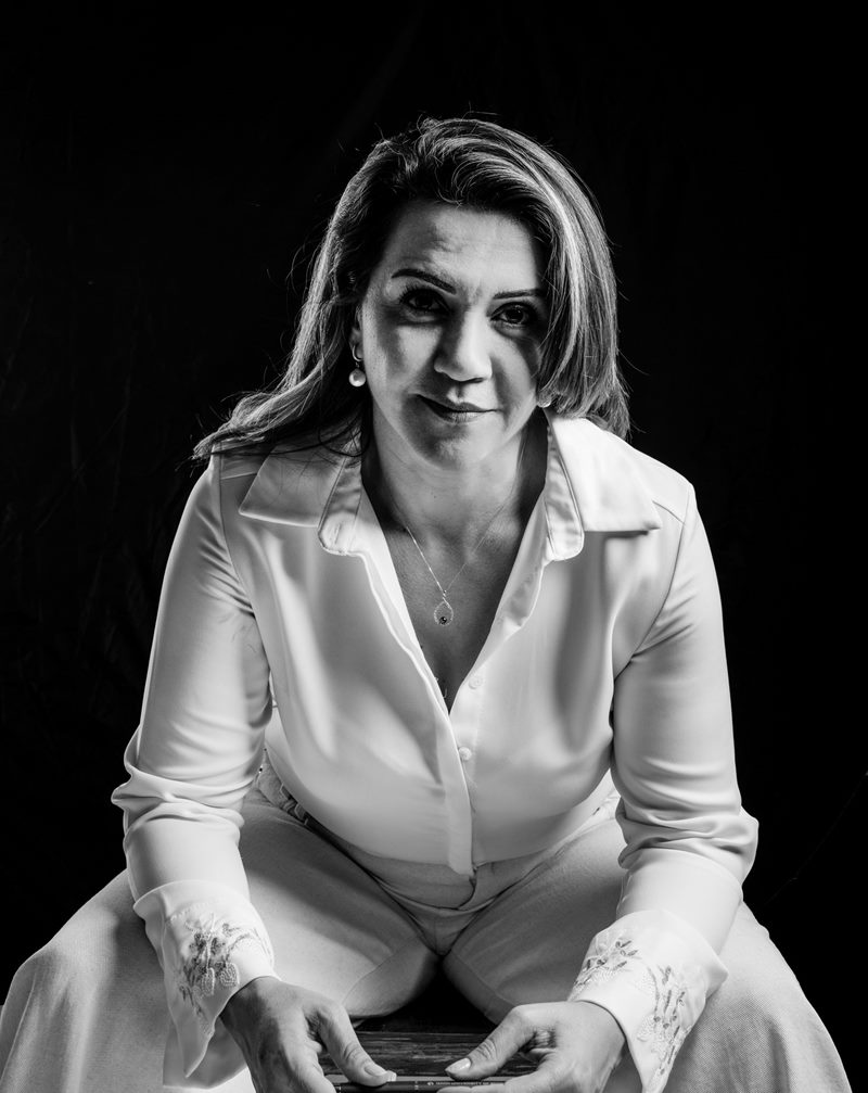 İzmir kurumsal portre fotoğraf çekimi koyu fonda öne eğilmiş kararlı bakışlı Dilara Karaçoban siyah-beyaz stüdyo portresi.