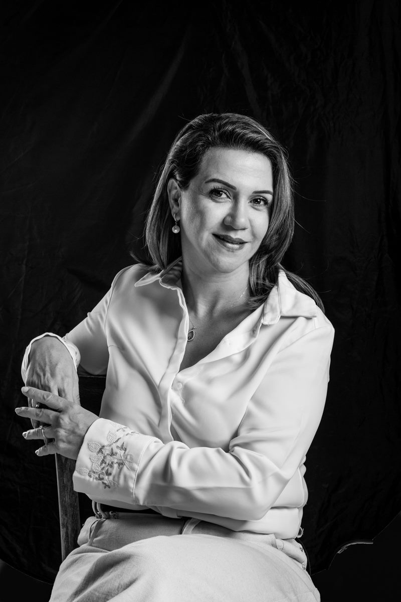 İzmir kurumsal portre fotoğraf çekimi sandalye arkalığına kolunu dayamış vakur bakışlı Dilara Karaçoban siyah-beyaz portresi.