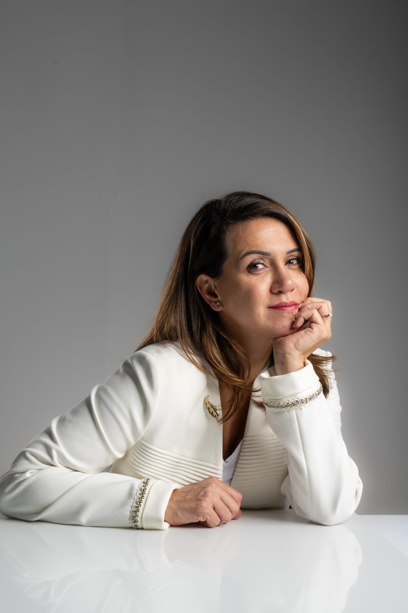 Dilara Karaçoban kişisel marka fotoğraf çekimi masada çenesini ellerine dayamış kadraj dışına bakan sakin renkli stüdyo karesi.