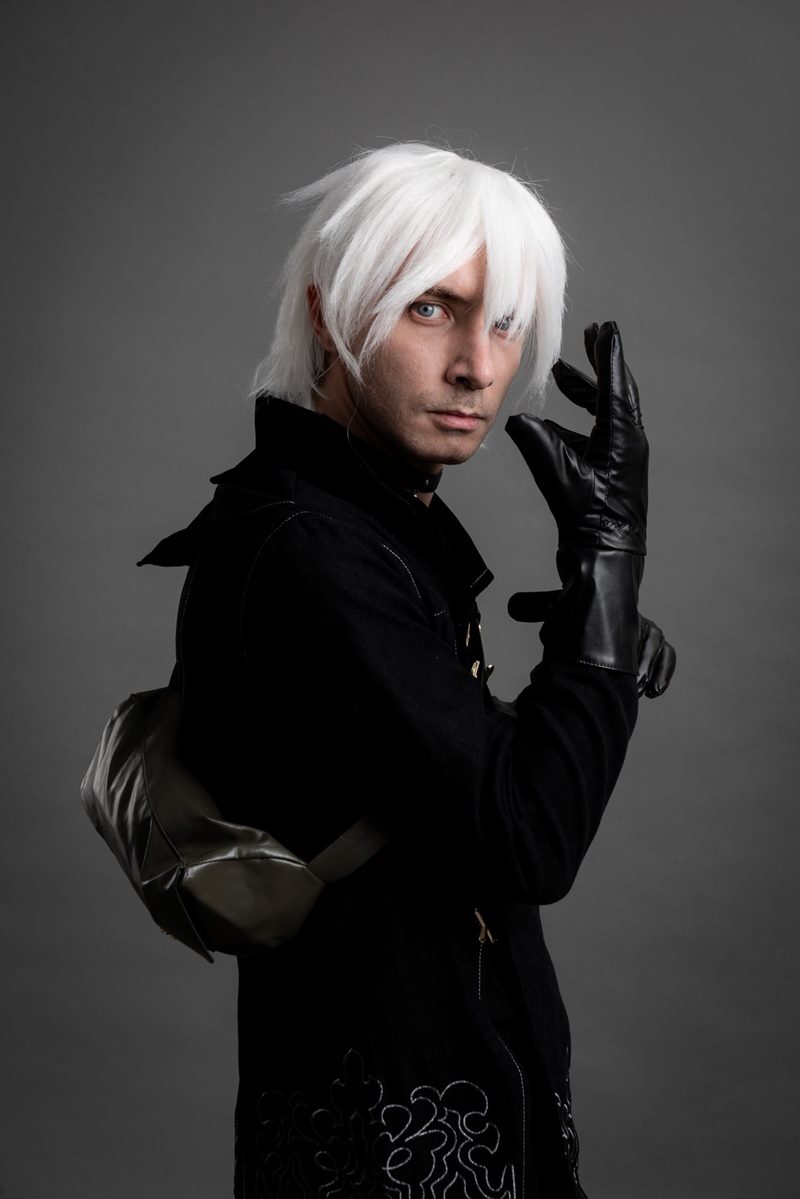 İzmir cosplay fotoğraf çekimi kapsamında gri fonda siyah deri eldivenli elini kaldıran NieR Automata 9S portresi.