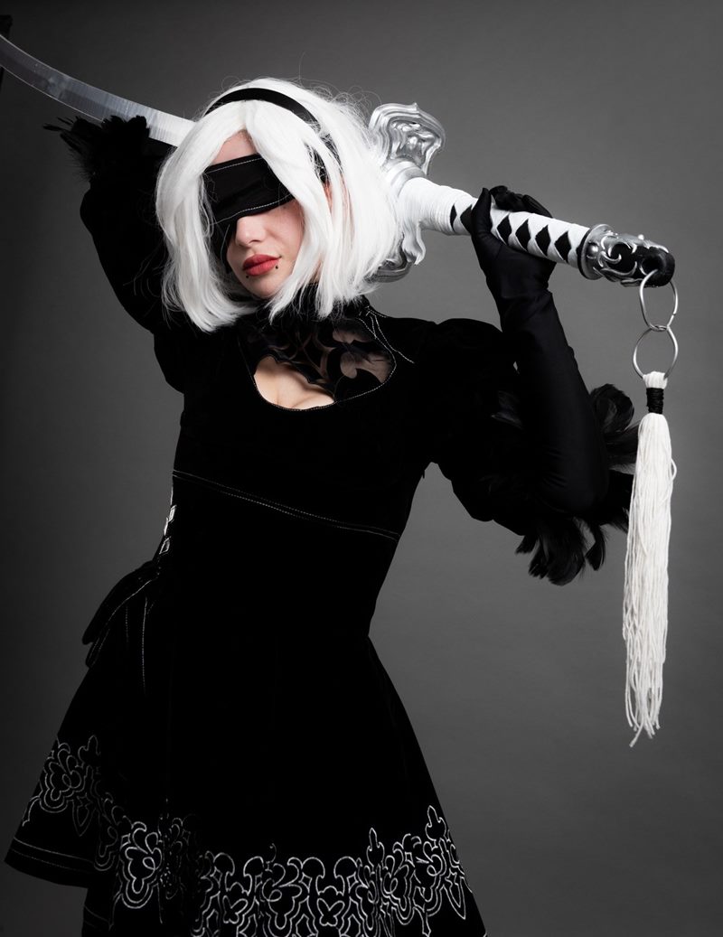 Gri kağıt fonda metalik kabzalı el yapımı kılıcını omzunda tutan göz bantlı 2B karakteri İzmir cosplay fotoğraf çekimi.