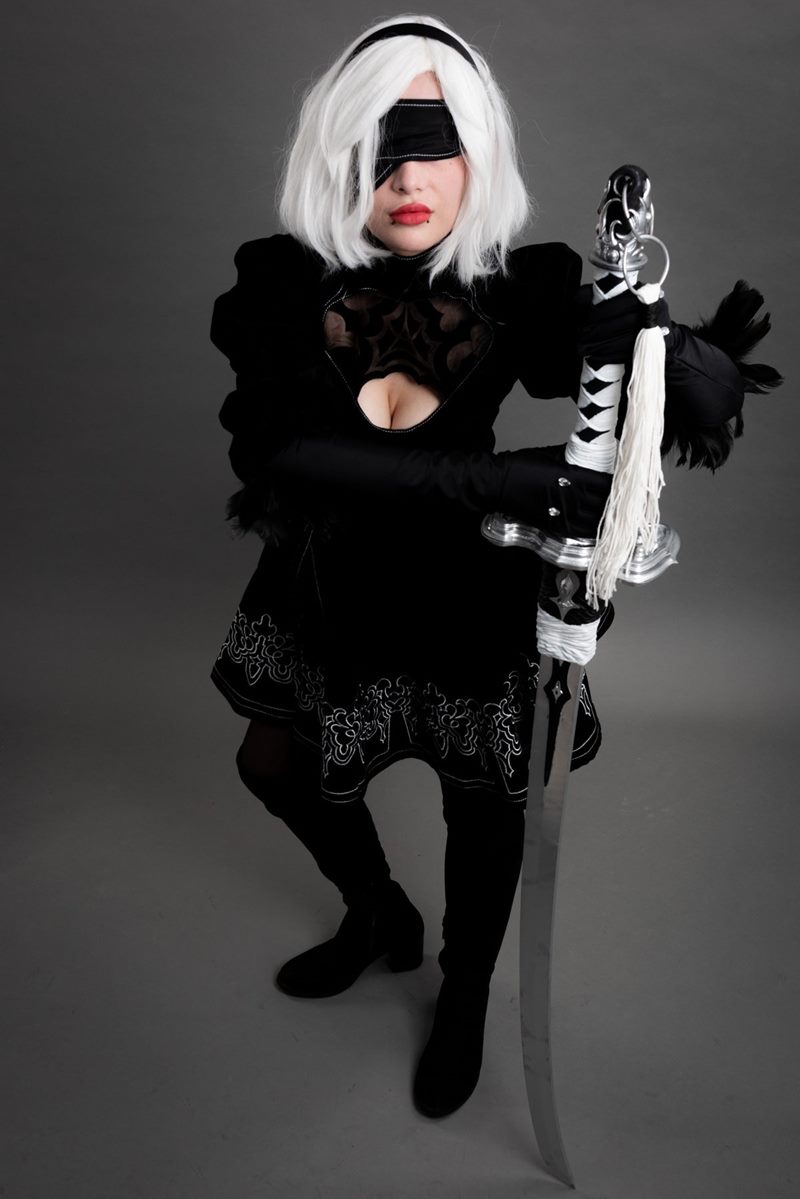 İzmir cosplay fotoğraf çekimi sırasında gri fonda el yapımı uzun kılıcını zemine dayayan göz bantlı 2B karakteri.