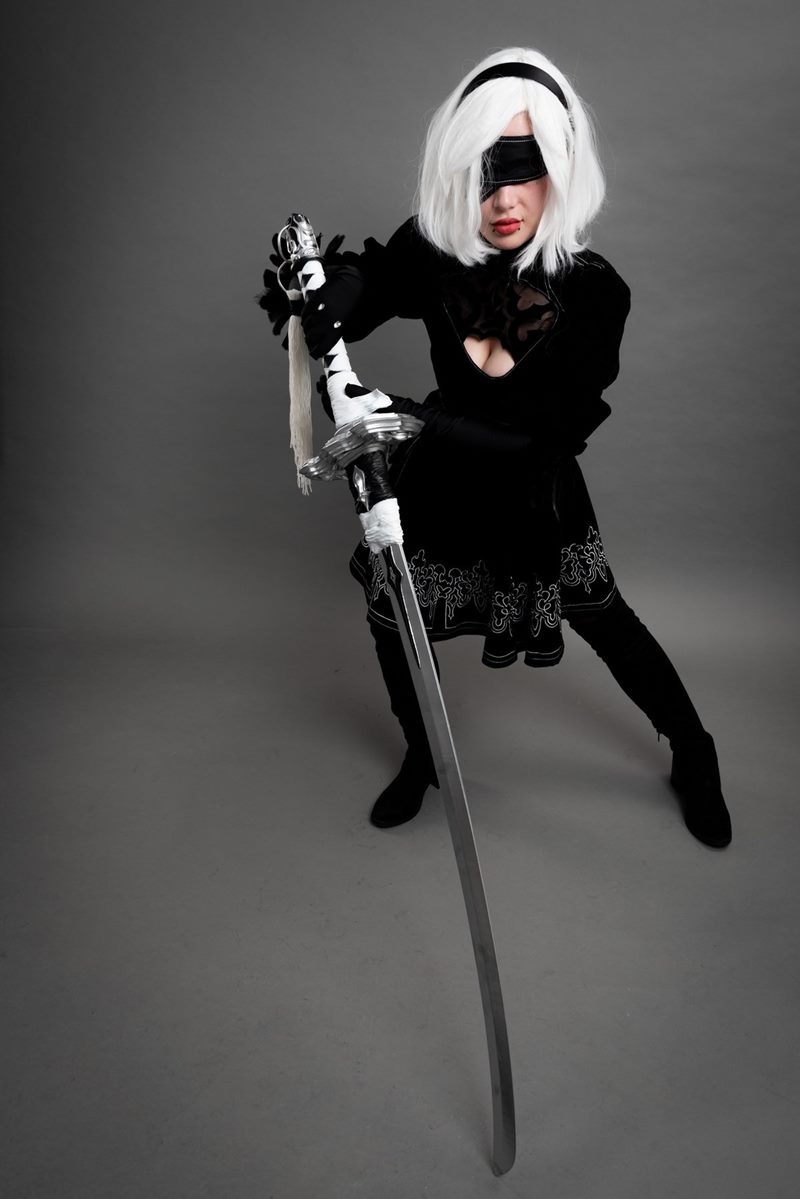 İzmir cosplay fotoğraf çekimi stüdyosunda uzun kılıcını öne doğru uzatarak poz veren göz bantlı 2B tam boy karesi.