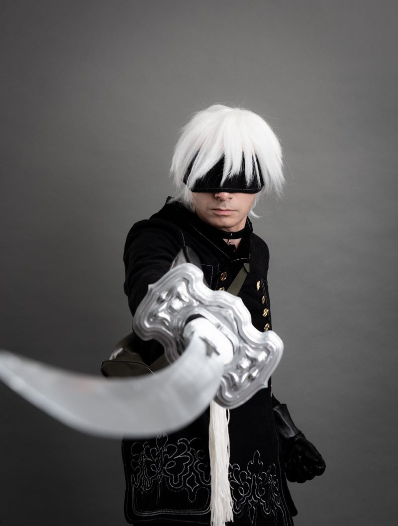 İzmir cosplay fotoğraf çekimi sırasında kılıcını doğrudan objektife doğru uzatan göz bantlı 9S stüdyo portresi.