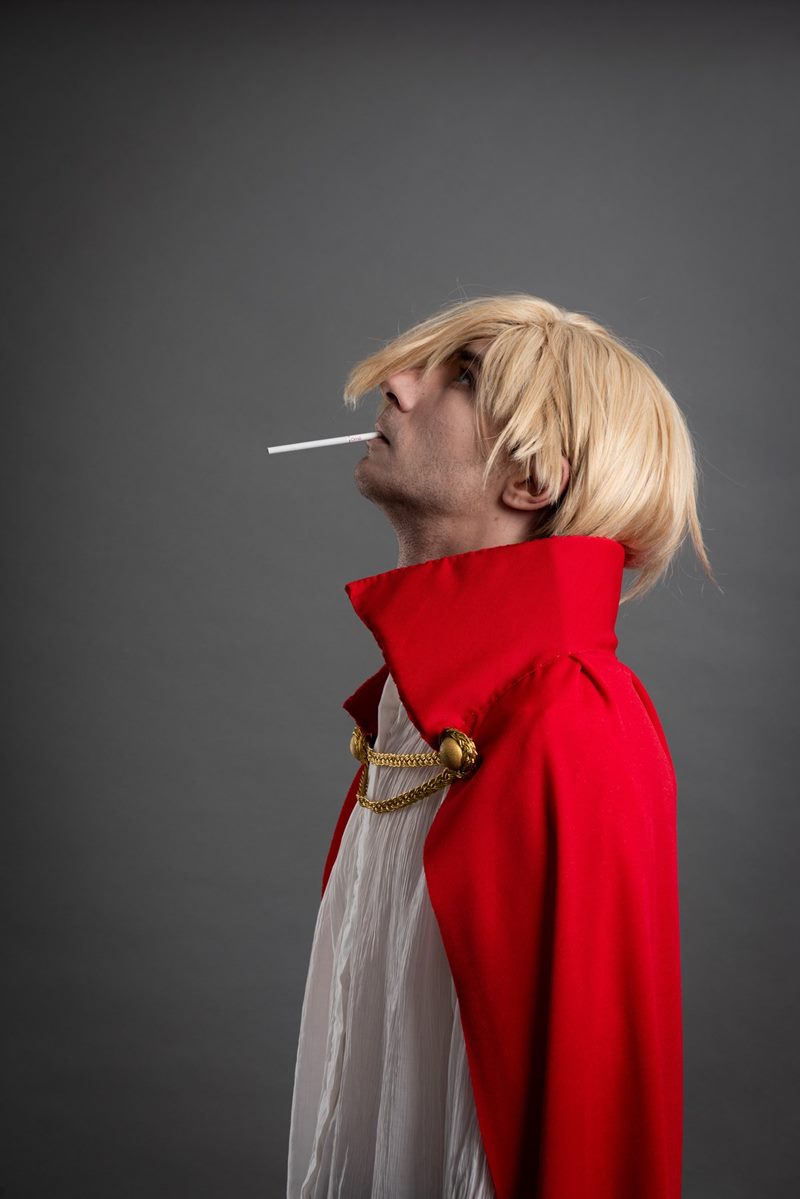 İzmir cosplay fotoğraf çekimi kapsamında gri fonda sarı peruklu ve kırmızı pelerinli modelin yan profil portresi.