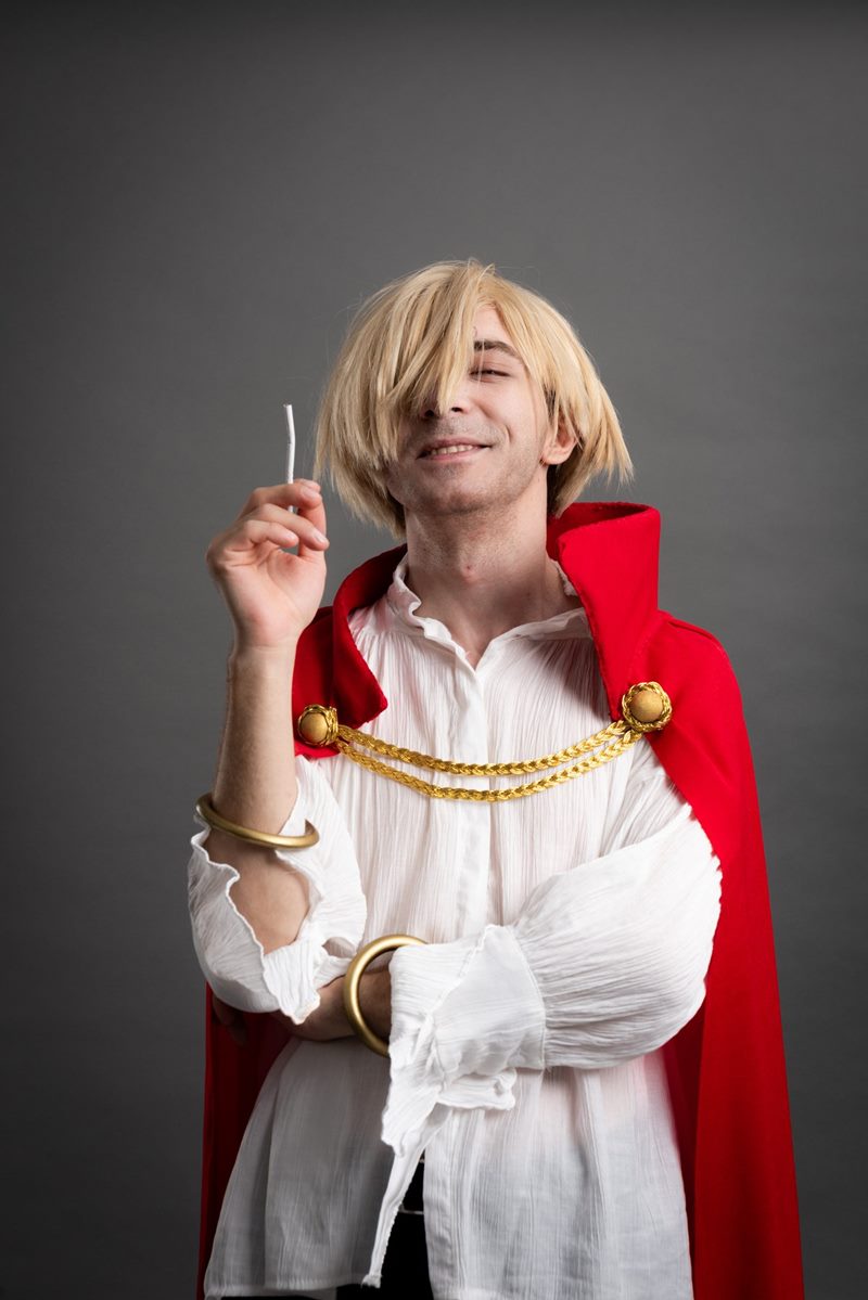 İzmir cosplay fotoğraf çekimi kapsamında gri fonda altın zincirli kırmızı pelerin ve sarı peruklu stüdyo portresi.